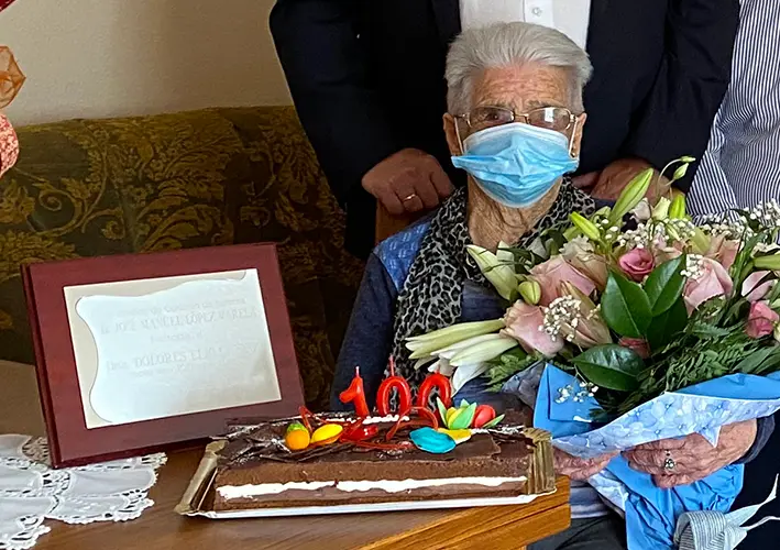 Dolores con las flores y junto a la placa conmemorativa de su aniversario